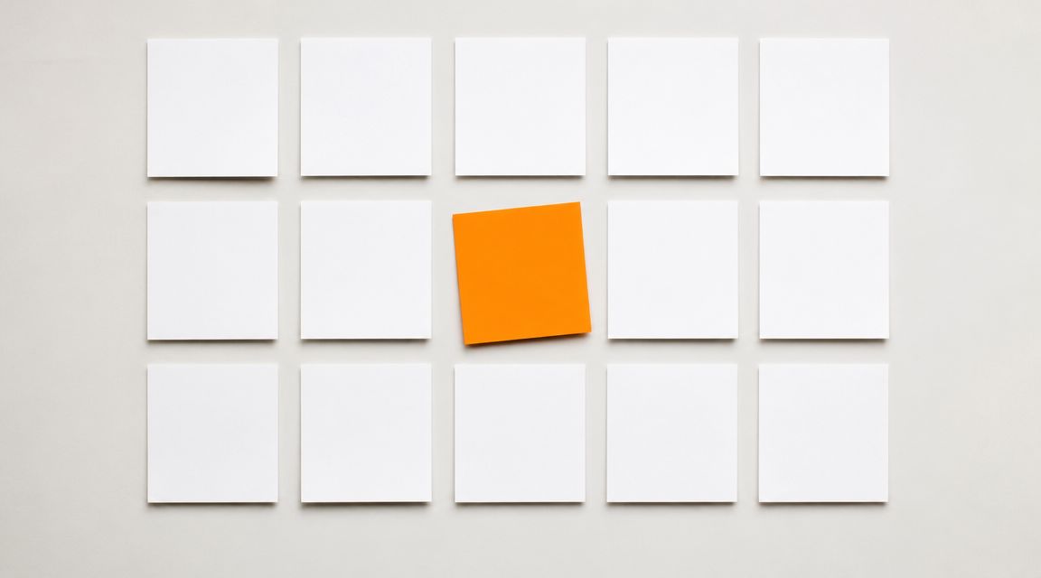 A grid of white sticky notes with a single vibrant orange note standing out in the center.