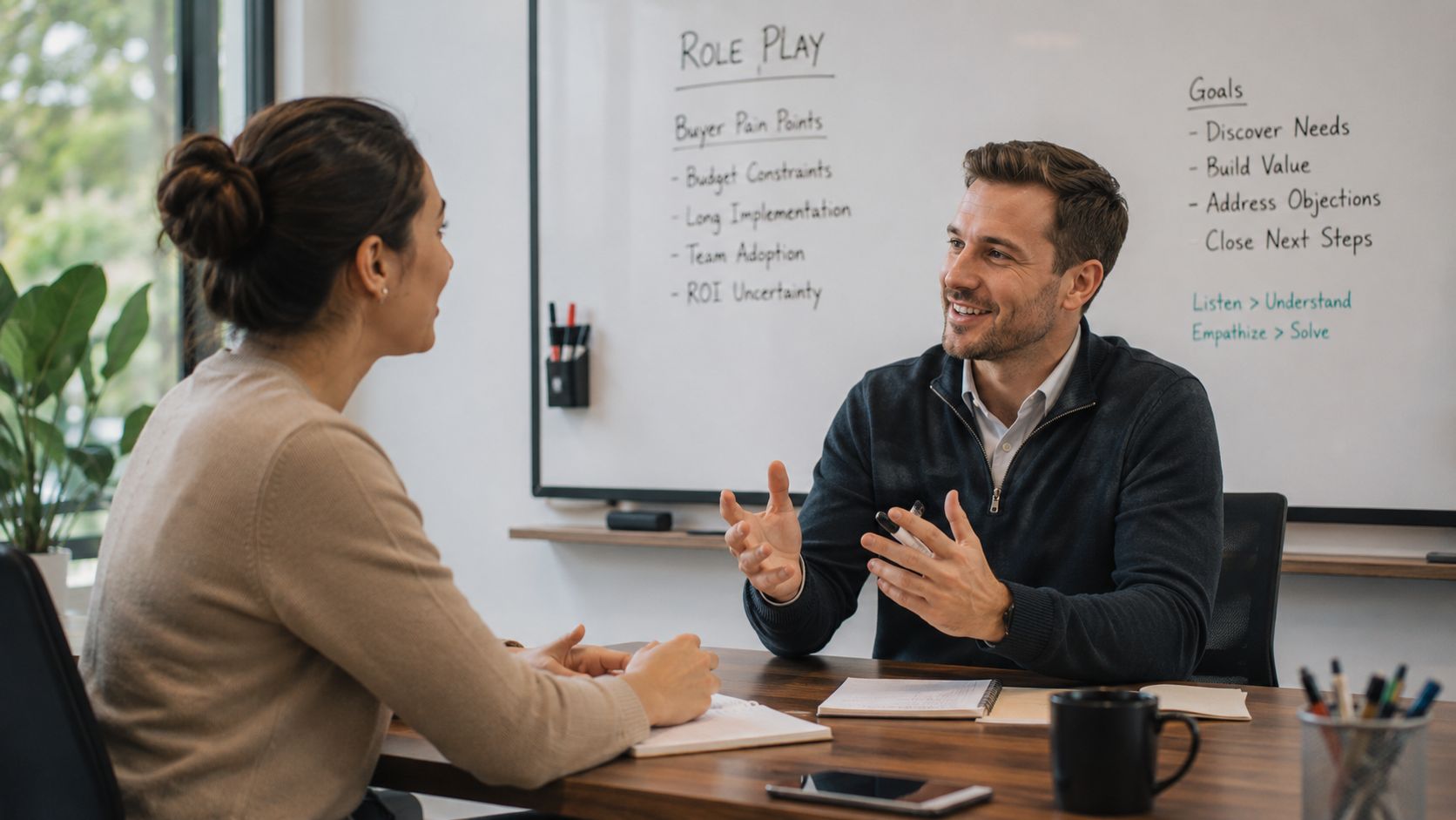 A professional man conducting a sales role play training session with a woman in an office.